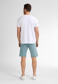Witte T-shirt met korte mouwen, lichtblauwe shorts en witte sneakers. Zachte stof, losse pasvorm en eenvoudig ontwerp zonder zichtbare patronen.