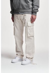 Béžové kordové cargo kalhoty s bočními kapsami, rovný střih a stahovací šňůrka na manžetách, spojené s bílými teniskami a šedou mikinou.