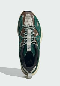 Scarpa sportiva con una parte superiore in mesh marrone, verde e grigio, dettagli testurizzati, lacci riflettenti e una suola imbottita di colore crema.