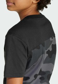 Black cotton T-shirt featuring a camouflage design in shades of gray, complete with short sleeves and a crew neckline.