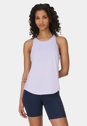 Woman with curly hair wearing a light purple sleeveless top and navy blue bike shorts, standing against a plain white background.