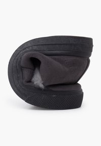 Zapato gris sin cordones con una parte superior suave y texturizada y suela flexible, que presenta un diseño enrollado que expone un interior peludo.