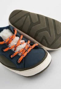 Marinblå och grön sneakers med klara orange och blå snören, texturerad sula och vita accenter. Mjuk innersula synlig nära snörena.