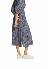 Náměsíčně modré šaty s bílým abstraktním vzorem, se třičtvrtinovými rukávy a splývavou sukní, doplněné bílými teniskami.