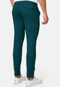 Pantalons extensibles teal avec une coupe fuselée, dotés de poches plates, d'une fermeture par bouton et d'une texture lisse. Associés à des baskets blanches.