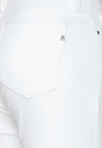 Jeans de mezclilla blanca que muestran un bolsillo trasero con un sutil acento de logo. El diseño presenta una textura suave y una forma ajustada.