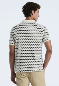 Kurzarm-Polohemd in Creme mit einem Diamantmuster in Marineblau. Verfügt über einen gerippten Kragen und Ärmelbündchen und zeigt eine enganliegende Passform.