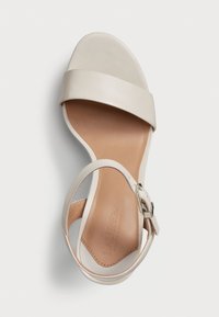 Beige lærsandaler med en bred tårem og en tynn ankelrem som har en spenne. Glatt tekstur og et beskjeden hældesign.