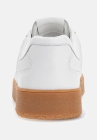 Witte sneaker met een glad leren bovenwerk, afgeronde vorm en een getextureerde lichtbruine rubberen zool. Heeft minimale stiksels en een trekhaak bij de hiel.