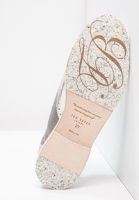 Semelle en suède gris avec des speckles blanches, accent en cuir beige, logo estampé et taille. Détails en dentelle délicate le long du bord.
