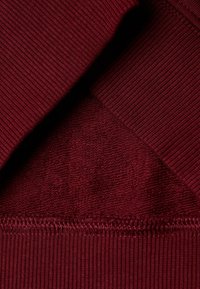 Bordeaux pletená tkanina s žebrovanými akcenty. Textura ukazuje kombinaci hladkých a mírně vyvýšených vzorů.