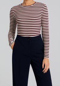 Maglietta a maniche lunghe a strisce orizzontali bordeaux e crema, abbinata a pantaloni navy a vita alta con bottone frontale e vestibilità sartoriale.