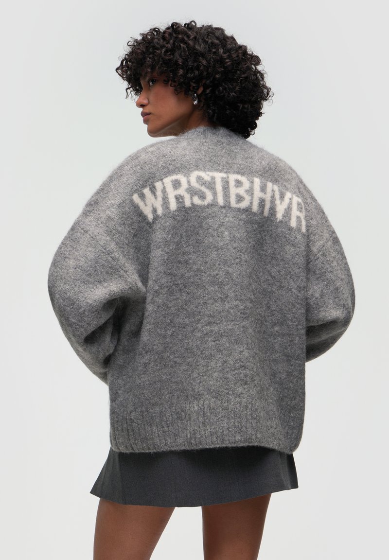 Grauer, übergroßer Pullover aus weichem Material mit dem Text "WRSTBHV" in heller Farbe auf der Rückseite. Strukturiertes, lockeres Design.