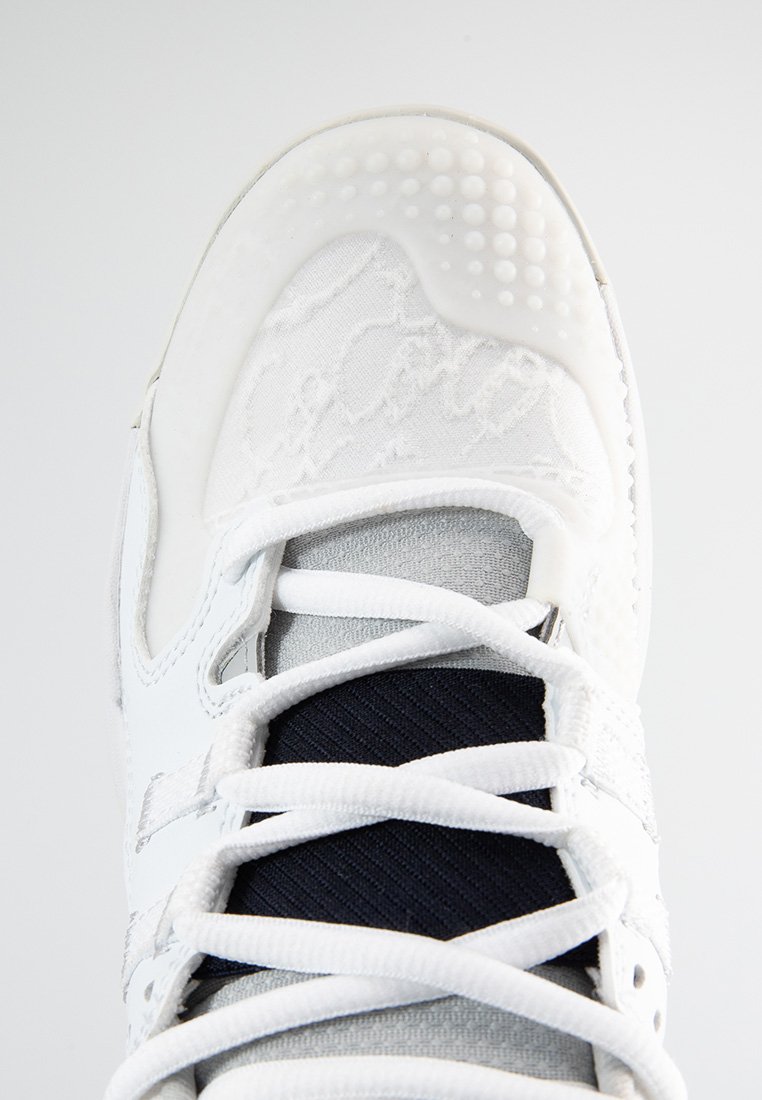 Chaussure de sport blanche avec un dessus texturé, des accents en tissu noir contrastants, un système de laçage bien visible et une semelle à pois pour assurer l'adhérence.