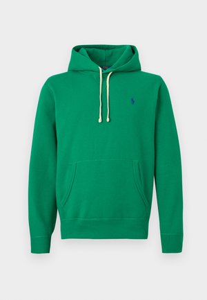 Zaļš džemperis ar kapuci, priekšējo kabatu, baltām auklām un mazu zilu izšūtu logo uz krūtīm, pret balta fona.