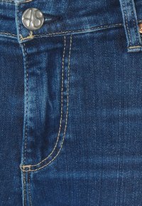 Mörkblå denimjeans med synlig knappstängning, ljusguldiga sömmar och en femfickdesign. Mjuk textur med lätt blekning.