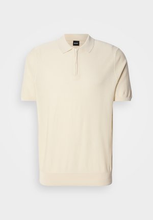 Kortærmet polo-shirt i lys beige, lavet af blødt strikmateriale. Har en halv-lynlås krave og en tætsiddende pasform med ribbet kant.