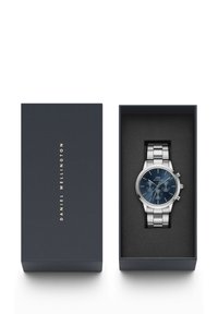 Orologio in acciaio inossidabile argentato con quadrante blu e dettagli argentati, esposto in una scatola blu scuro con branding minimalista.