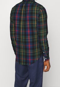 Koszula w kratę z guzikami w kolorach zielonym, niebieskim, czerwonym i żółtym. Długie rękawy, zaokrąglony dół oraz białe guziki przy mankietach. Teksturowany materiał.