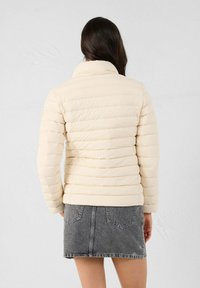 Crème kleurige pufferjack met een gestikt ontwerp, hoge kraag en lange mouwen, gecombineerd met een grijze denim rok. Soepele textuur, casual pasvorm.