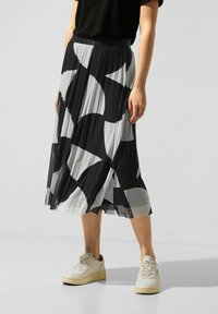 Svartvitt plisserat midja med ett geometriskt mönster, tillverkat av lättviktigt tyg, kombinerat med beige sneakers för en avslappnad look.