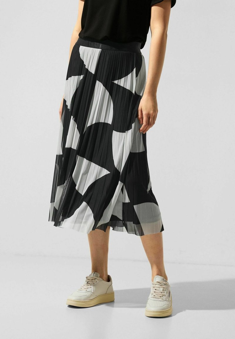 Svartvitt plisserat midja med ett geometriskt mönster, tillverkat av lättviktigt tyg, kombinerat med beige sneakers för en avslappnad look.