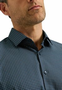 Kurzarmhemd in Marineblau mit einem geometrischen Muster aus kleinen weißen und hellblauen Quadraten. Verfügt über einen klassischen Kragen und eine Knopfverschluss.