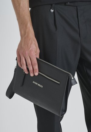 Clutch negro texturizado con un bolsillo con cremallera en la parte frontal y herrajes de acero inoxidable. Presenta el nombre de la marca "ANTONY MORATO" grabado en la parte frontal.