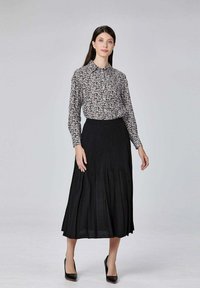 Jupe midi plissée noire associée à une chemise à boutons blanche et noire à motifs. Le mannequin porte des chaussures à talons noirs. Texture lisse.