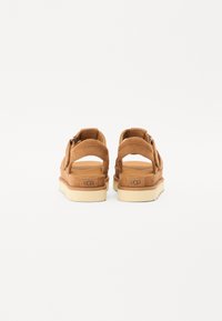 Brune semskede sandaler med justerbar remdesign, med en lys beige sål og UGG-merke på hælen. Bakken.
