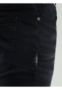 Jeans in denim nero con una vestibilità slim, una texture sottile e un piccolo etichetta "CHASIN'" sulla tasca laterale. Componenti in metallo argentato.