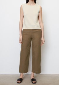 Top beige senza maniche, pantaloni larghi verde oliva, sandali neri a scivolo. Texture liscia, design semplice, orlo cropped sul top, pantaloni dalla vestibilità comoda.