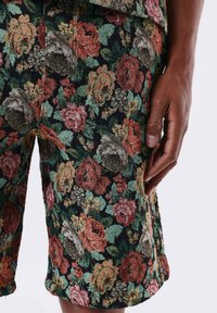 Shorts floraux avec un tissu texturé sur fond sombre. Les couleurs dominantes incluent des fleurs rouges, orange, vertes et roses intégrées dans le design.