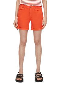 Shorts en denim orange avec des revers, dotés de poches avant et d'une fermeture à un seul bouton en métal. Associés à des sandales noires à lanières.