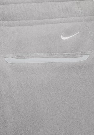 Gros plan sur un vêtement en polaire gris avec une poche zippée et le logo Nike swoosh blanc au-dessus de la poche.