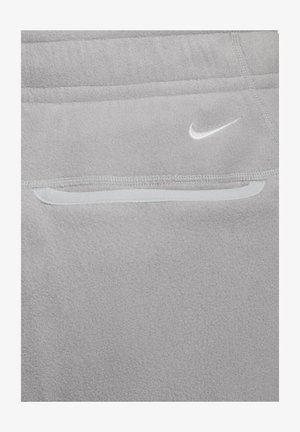 Κλείσιμο ενός γκρι ρούχου από φλίς με τσέπη με φερμουάρ και λευκό λογότυπο Nike Swoosh πάνω από την τσέπη.