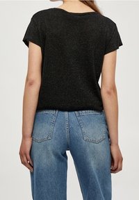 Černé tričko s krátkým rukávem a kulatým výstřihem, vyrobené z texturované látky, spárované s vysoce pasovými světle modrými džínami.