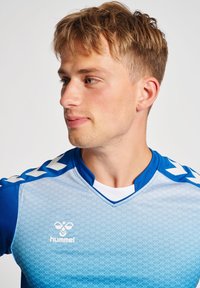 Blå gradient sportsjerso med geometrisk mønster, Hummel-logo på brystet og karakteristiske hvide chevron-accenter på skulderne.