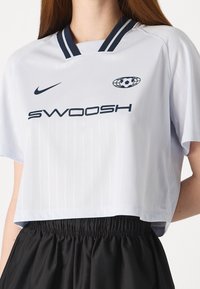 White cropped sports jersey with vertical stripes, navy accents, a v-neckline, and logo details from Nike and SWOOSH. Soft fabric.