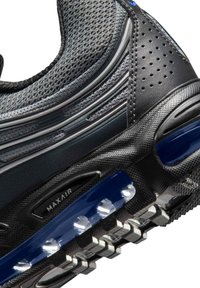 Zapato deportivo negro con parte superior de malla con detalles en gris, acentos en azul, amortiguación Max Air y suela de goma texturizada con tacos.