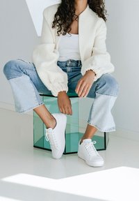 Biała teksturowana kurtka z balonowymi rękawami, w połączeniu z białym topem na ramiączkach i jasnoniebieskimi krótkimi jeansami. Dopełnieniem stylizacji są białe trampki.