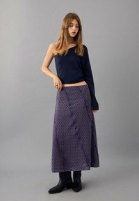 Navy one-shoulder sweater, paired with a long, patterned skirt featuring circles in red and blue. Black ankle boots complete the look.