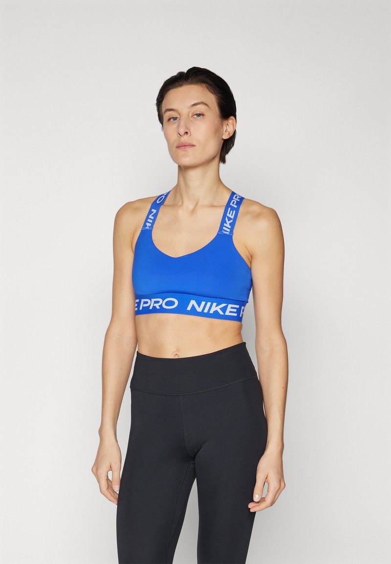 Zila sporta krūšturis ar Nike logotipu baltos krāsas tekstā uz siksnām un joslas; gluda, elastīga auduma; savienots ar augstās jostasvietas melnām legingām.