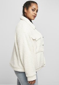 Hvit, luftig skjermjakke med krage, knappelukking og frontlommer. Designet har en løs passform med myk, teksturert stoff.
