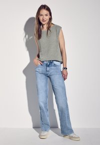 Top de punto sin mangas en gris claro combinado con jeans rectos en azul claro; la modelo está de pie con una mano en el bolsillo, usando zapatillas claras.