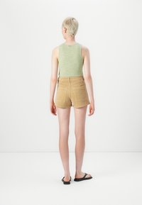 Green ribbed tank top, khaki corduroy shorts with back pockets, and black flip-flops, viewed from the back against a white background.