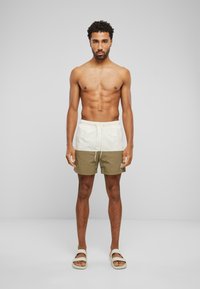 Maillots de bain pour hommes avec un design coloré, présentant une partie supérieure blanche et une partie inférieure vert olive. Tissu léger et taille ajustable.