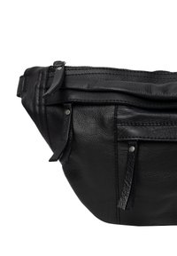 Musta nahkavyölaukku, jossa on tekstuuripinta, vetoketjullinen yläosa, etutaskut ja koristeelliset tupsut. Kestävä ompelu ja metalliset yksityiskohdat.