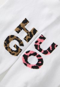Baltos kojinės su didelėmis raidėmis "G" ir "O" gyvūnų raštu: "G" rudos leopardų spalvos ir "O" rožinės bei juodos leopardų raštų.