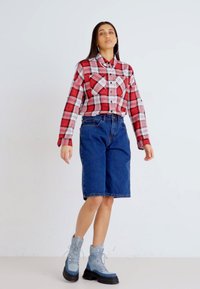 Chemise en flanelle à carreaux rouges et blancs, shorts en denim bleu et bottes à lacets grises. La tenue présente une coupe décontractée et des textures douces.